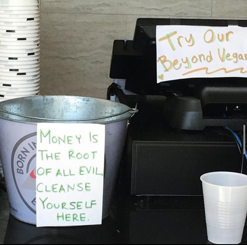 a cash register with a tip jar next to it. On the tip jar is a handwritten sign that says 'money is the root of all evil, cleanse yourself here.'